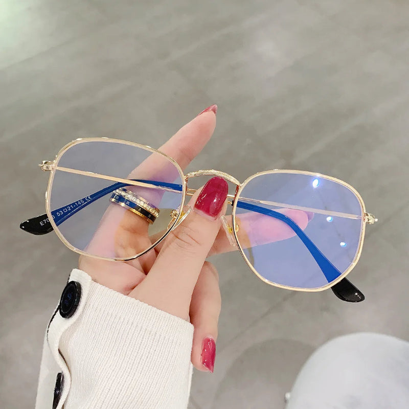 Woman holding Blue Light Glasses Zoe with Gold metal frame. Designed to reduce eye strain from screens and improve visual comfort. Lightweight and elegant square shape with thin, durable temples. Adjustable nose pads for a secure and comfortable fit. Clear, anti-reflective lenses block harmful blue light while maintaining style and sophistication. Ideal for use with computers, phones, and tablets. Stylish unisex design, perfect for everyday wear or professional settings. Discover more at www.zenluk.com