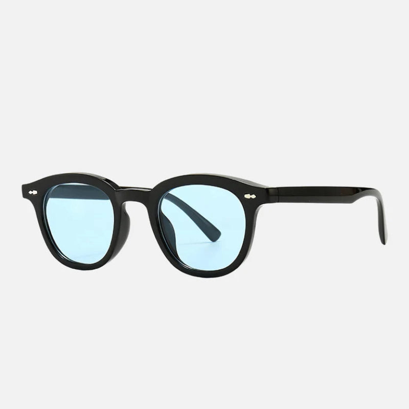 Sunglasses George Blue with a glossy black acetate frame and round blue-tinted lenses, shown from a three-quarter angle to display the temple design and polished finish. The silver rivet details on the front corners add a subtle touch of sophistication. Perfectly captured on a white backdrop for a refined, modern look. Visit www.zenluk.com
