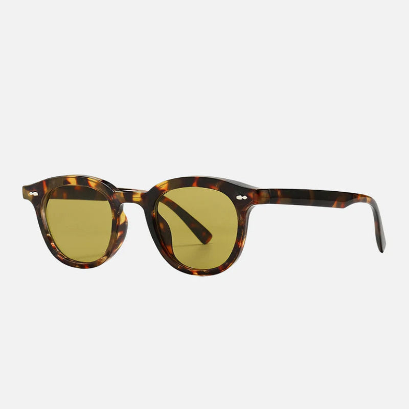 Sunglasses George Leopard – Angled side view of trendy round sunglasses with a glossy leopard-patterned frame in rich brown and golden hues. The yellow-tinted lenses bring a retro yet modern vibe, while the slightly curved temples provide a comfortable fit. Perfect for adding a pop of personality to any outfit. Shop now at www.zenluk.com
