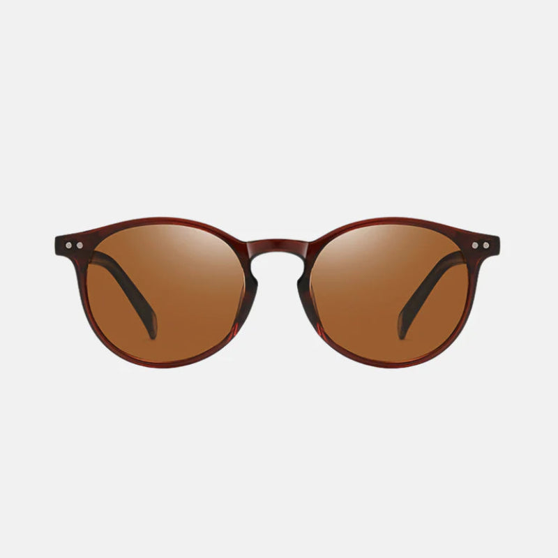 Sunglasses Lico Brown, featuring a full-rim round frame in deep brown acetate with a polished finish. The front view highlights the warm brown-tinted lenses with a subtle mirror effect, complemented by two small metallic rivets on each upper corner of the frame. The temples are slim and matching in brown for a cohesive and elegant look. www.zenluk.com