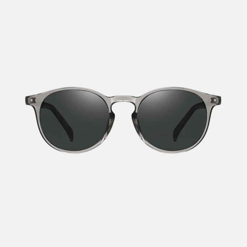 Sunglasses Lico Grey – sleek round-frame sunglasses in a transparent grey acetate finish, featuring solid dark grey polarized lenses. The frame has a subtle glossy surface, with metal rivet details near the hinges for a refined touch. The nose bridge is molded for comfort, and the straight temples maintain the transparent grey design. Displayed on a white background, front-facing view. www.zenluk.com