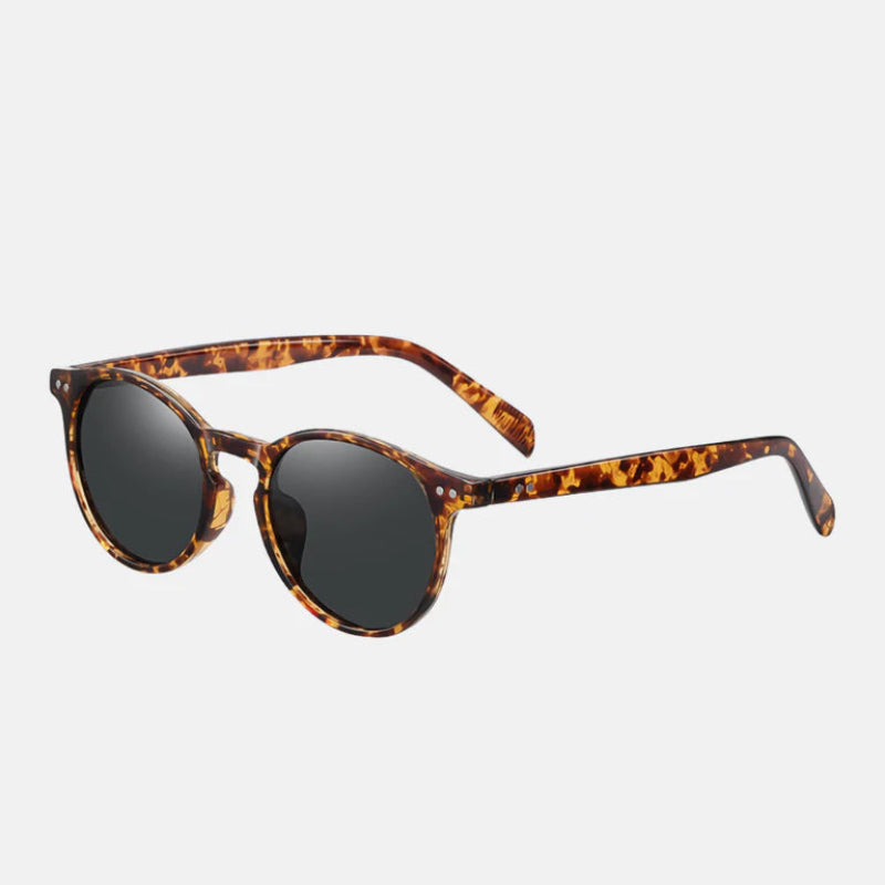 Sunglasses Lico Leopard – side view showing the round tortoiseshell frame with warm amber and dark brown mottled tones. The dark polarized lenses provide a sleek contrast. The temples extend smoothly from the front frame with matching tortoiseshell coloring and a glossy finish. Visible silver rivet details near the hinges enhance the vintage-inspired style. The image highlights the curvature of the arms for a comfortable fit. Displayed against a minimal light background for clarity. www.zenluk.com