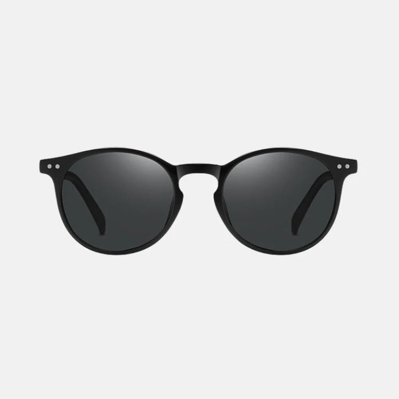 Sunglasses Lico Black – Sleek matte black round frame with a slightly keyhole-shaped bridge. Features double silver rivets on each upper corner of the frame and matching black temples with a subtle glossy finish. The lenses are dark black, providing full UV protection, and the background is plain light grey for a clean presentation. www.zenluk.com