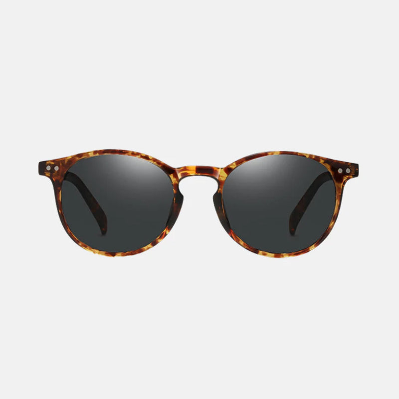 Sunglasses Lico Leopard – round frame in a rich tortoiseshell pattern combining warm amber, brown, and honey tones. The dark polarized lenses offer full coverage, with subtle silver rivet details on each upper corner of the front frame. The nose bridge is slightly arched, giving a classic and elegant look. The arms match the tortoiseshell pattern and feature the same silver rivet accents near the hinges. Displayed against a clean light background for a crisp, professional product view. www.zenluk.c