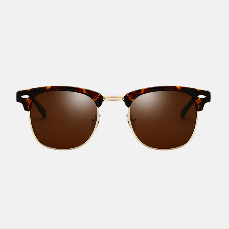Sunglasses Ruby in tortoiseshell brown with a semi-rimless design. The top frame features a rich tortoiseshell acetate with gold metallic accents, while the bottom half of the lenses is rimless for a refined look. The lenses are a warm brown tone, offering UV protection with a sophisticated style. The bridge and nose pads are gold, adding a luxurious touch. Discover more at www.zenluk.com