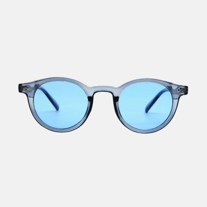 Sunglasses Vero Blue – round frame in transparent light blue acetate, featuring sleek integrated nose bridge and subtle metallic hinge detailing. The lenses are a vibrant mirrored blue, reflecting light with a crisp, modern aesthetic. The temples are slim, matching the frame’s transparent blue tone. Minimalist white background highlighting every design detail. www.zenluk.com