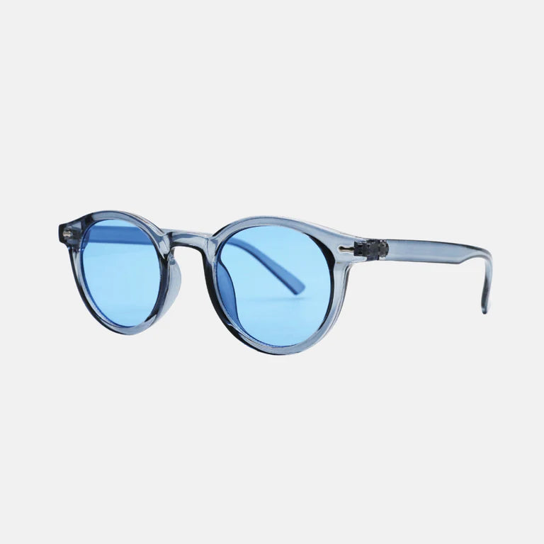 Sunglasses Vero Blue – round frame in transparent light blue acetate, shown from a three-quarter side view revealing the smooth curvature of the temples and precision hinge construction. The vivid mirrored blue lenses enhance the contemporary and stylish look, while the clean white background emphasizes the premium finish. www.zenluk.com