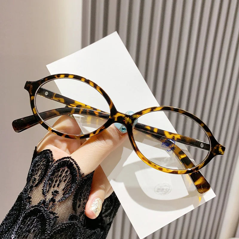 Woman Holding Blue Light Glasses Shine with Leopard tortoiseshell frame, oval-shaped design and clear blue light filter lenses. Lightweight and stylish, these glasses reduce eye strain, improve sleep, and protect your eyes from harmful screen glare. Ideal for long hours in front of computers, phones, and tablets. Comfortable for everyday wear with a premium look and smooth fit. Available now at www.zenluk.com